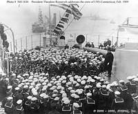 President Theodore Roosevelt (standing on 12" gun turret at right) addresses officers and crewmen on the after deck of USS 